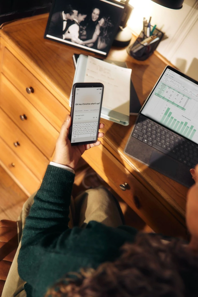 Persona sosteniendo un teléfono cerca de una laptop y una tableta en un escritorio